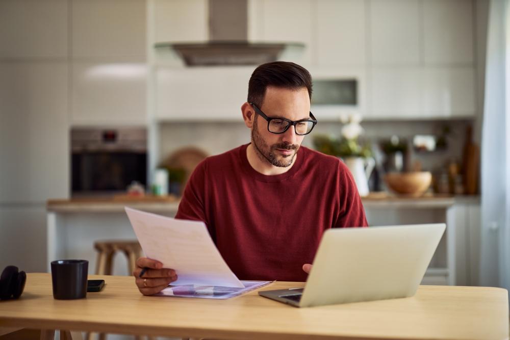 A man sits at a computer and reviews his finances while wondering at what age he needs a will.
