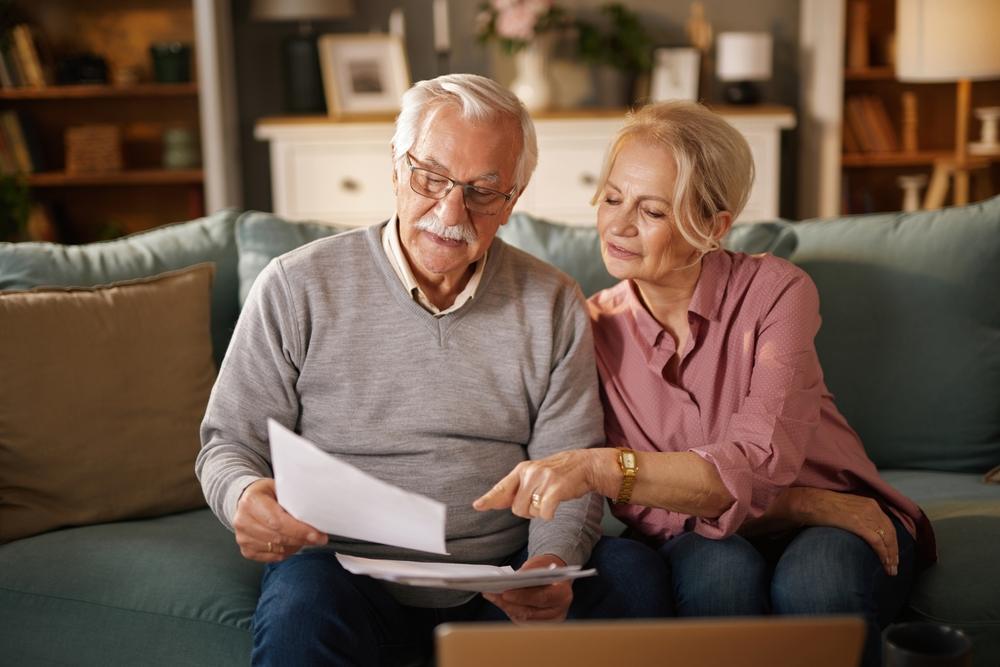 An older couple sits on a couch and reviews documents to learn what an advance directive for healthcare is.
